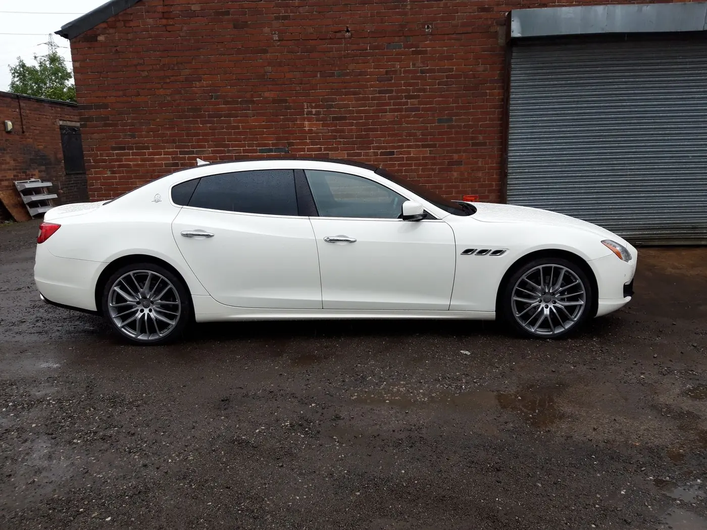 A white Maserati Quattroporte on our gravel yard, in front of the brick wall and roller shutter